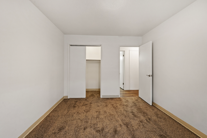 Bedroom with white walls, brown carpet, and a closet