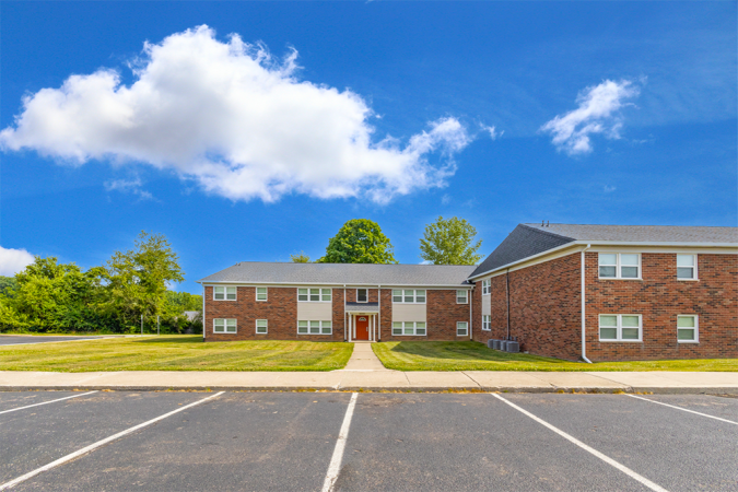 Brick apartment building with a front yard and parking lot